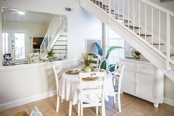 A dining area with a white table, chairs, and a staircase.
