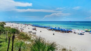 Een strand met wit zand, blauwe parasols en helderblauw water.
