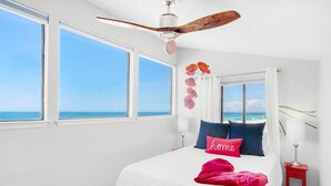 Een slaapkamer met een groot bed, een plafondventilator en uitzicht op de oceaan door grote ramen.