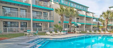 A hotel with a swimming pool, multiple balconies, and lounge chairs.