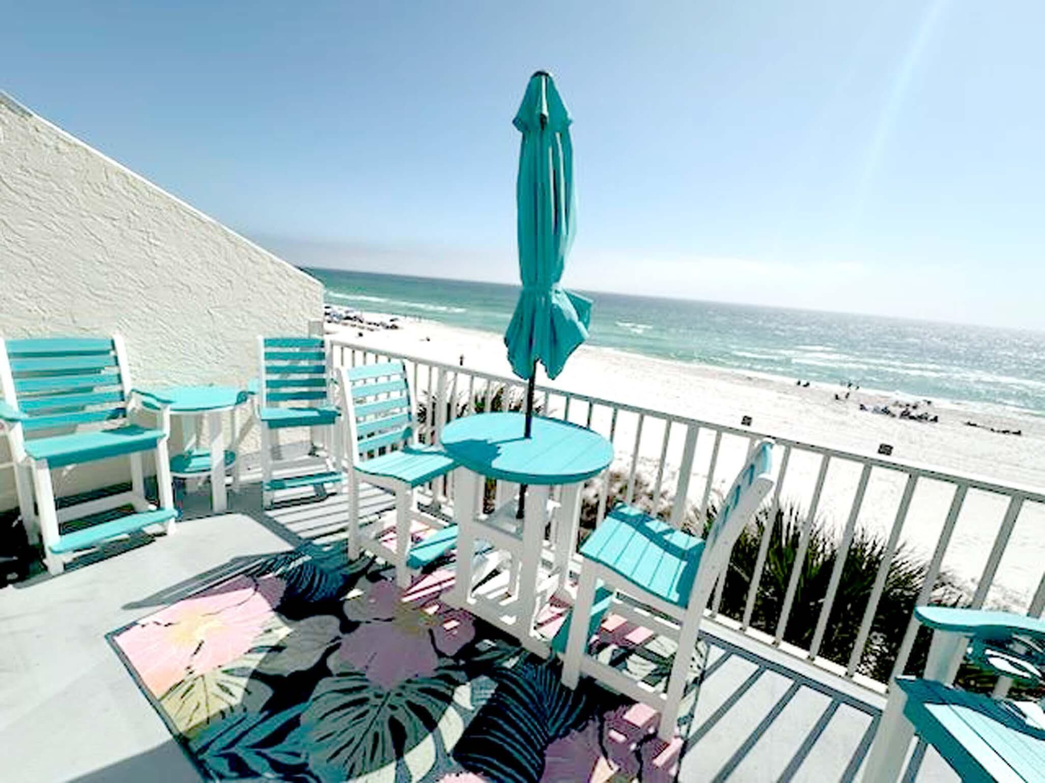 A balcony with turquoise chairs and a table, overlooking a beach.