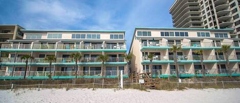 A beachfront hotel with multiple balconies, a sandy beach in front, and a clear sky.