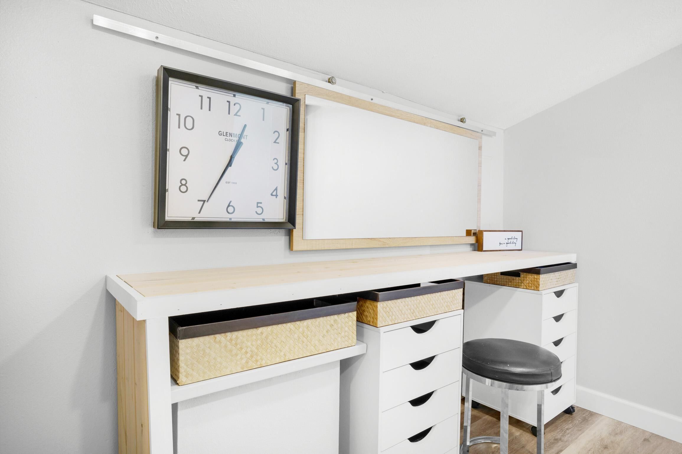 A modern room with a white desk, a clock, and a whiteboard.