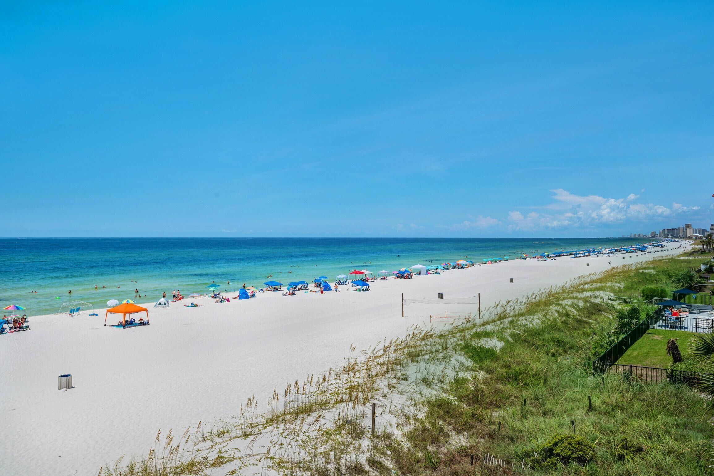 Ein weiter Sandstrand mit klarem, blauem Wasser, Sonnenschirmen und Menschen.