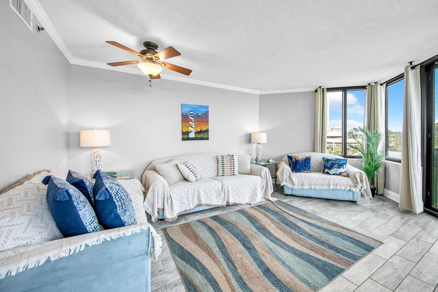A modern living room with a ceiling fan, two sofas, a patterned rug, and large windows offering a view.