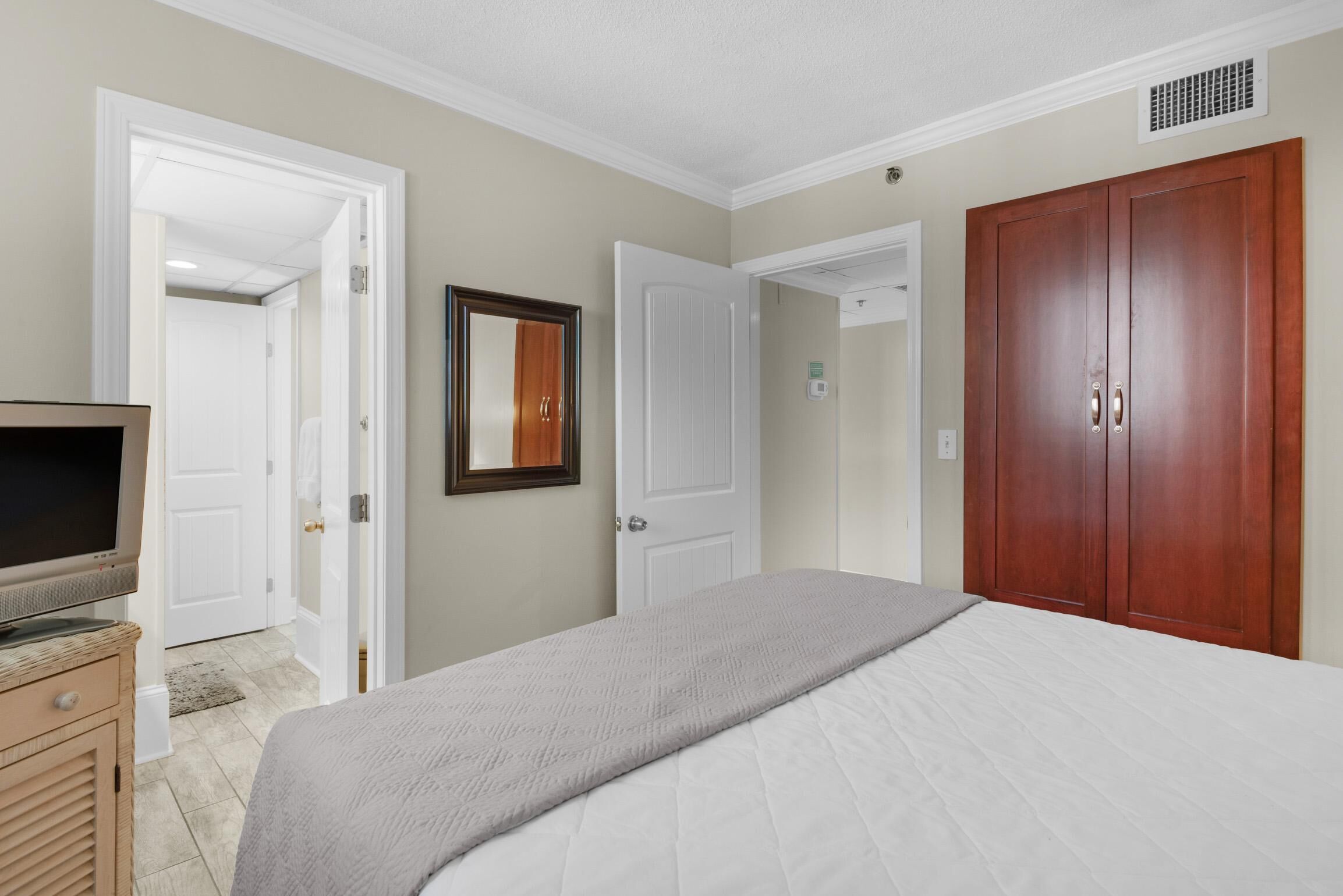A bedroom with a bed, a television on a dresser, and a wardrobe.