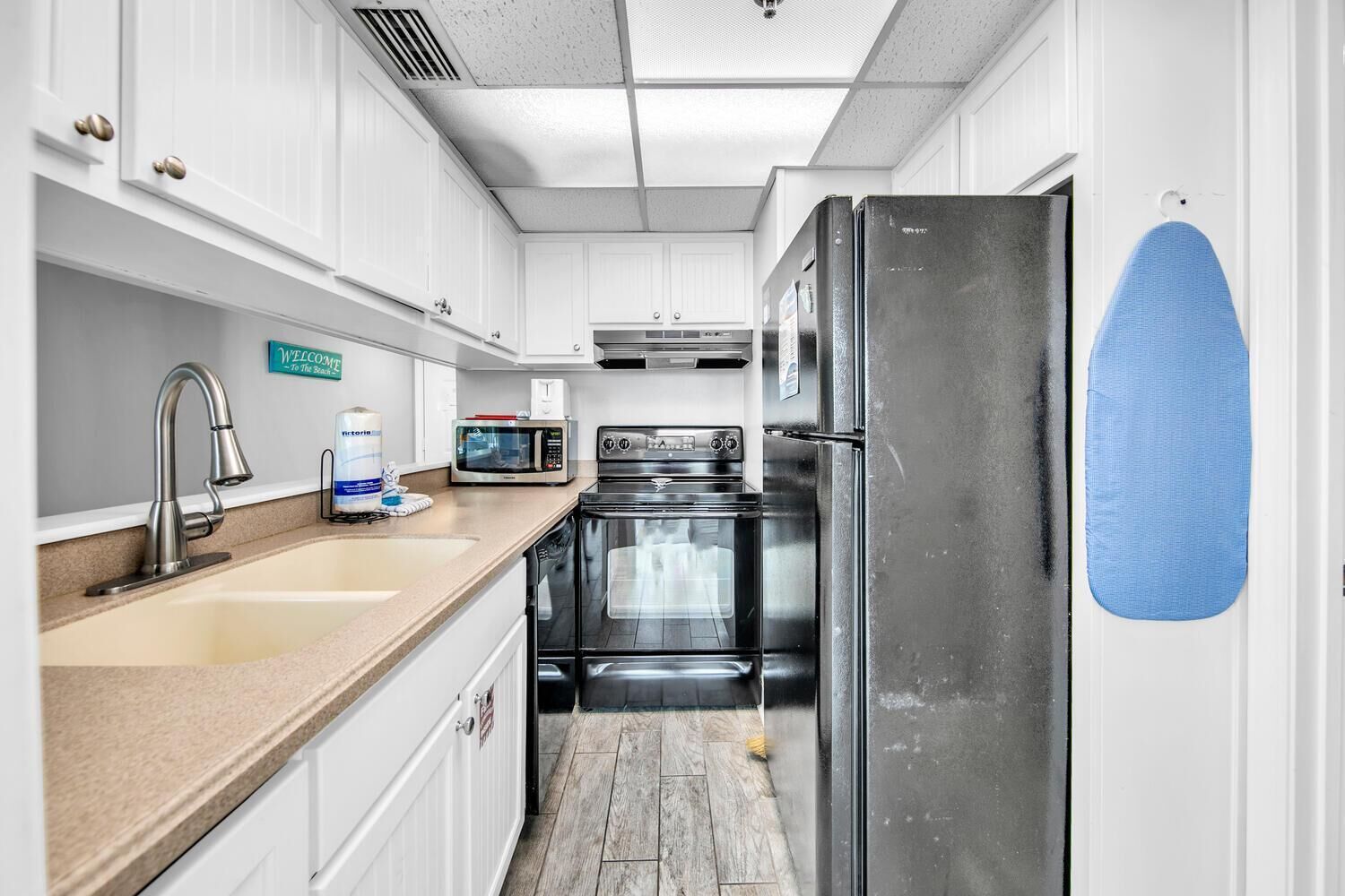 A compact kitchen with white cabinetry, a stainless steel refrigerator, a microwave, a stove, and a sink.