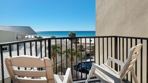 En balkong med två vita stolar, en pool och utsikt över stranden och havet.