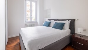 Un dormitorio con cama, mesita de noche, ventana y radiador.