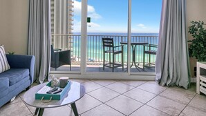 A balcony with a view of the ocean, a sofa, a table with a tray, and a potted plant. - Shores of Panama 1212 (Panama City Beach)