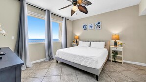 A bedroom with a large bed, a desk, a ceiling fan, and a view of the ocean. - Shores of Panama 1212 (Panama City Beach)