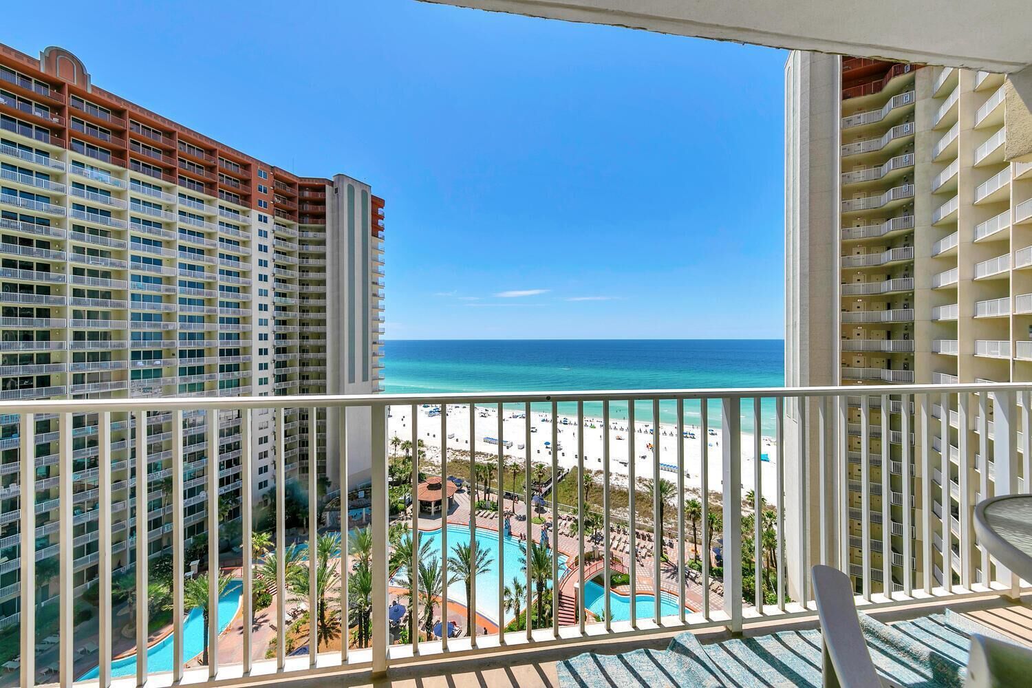 A high-rise hotel with multiple balconies overlooking a beach and a pool area.