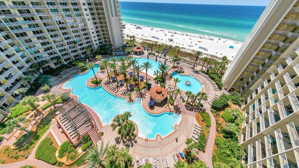 A resort with a central pool surrounded by palm trees and lounge areas, overlooking a beach. - Shores of Panama 1212 (Panama City Beach)
