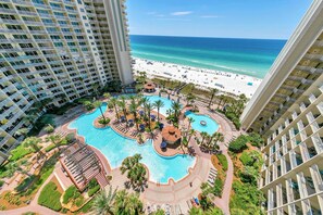 A resort with a central pool surrounded by palm trees and lounge areas, overlooking a beach. - Shores of Panama 1212 (Panama City Beach)