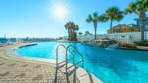 A swimming pool with a sunlit sky, palm trees, and a white fence.