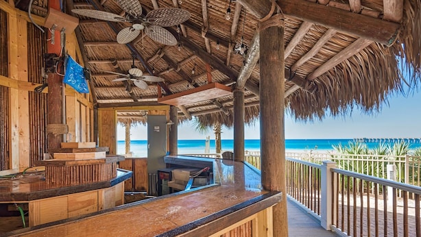 A wooden bar area with a thatched roof, overlooking a beach. - Calypso 3-504 (Panama City Beach)