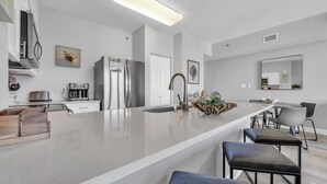 A modern kitchen with a central island, stainless steel appliances, and a dining area with bar stools. - Shores of Panama 2004 (Panama City Beach)