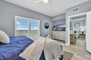 A bedroom with a bed, a dresser, a TV, and a view of the outdoors.