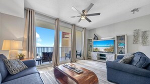 A modern living room with a large TV, two sofas, a wooden coffee table, and a balcony with a view. - Shores of Panama 2004 (Panama City Beach)