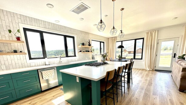 Een moderne keuken met een centraal eiland, groene keukenkastjes en grote ramen.