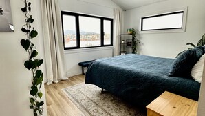 Een slaapkamer met een bed, een houten nachtkastje, een raam en een plant.