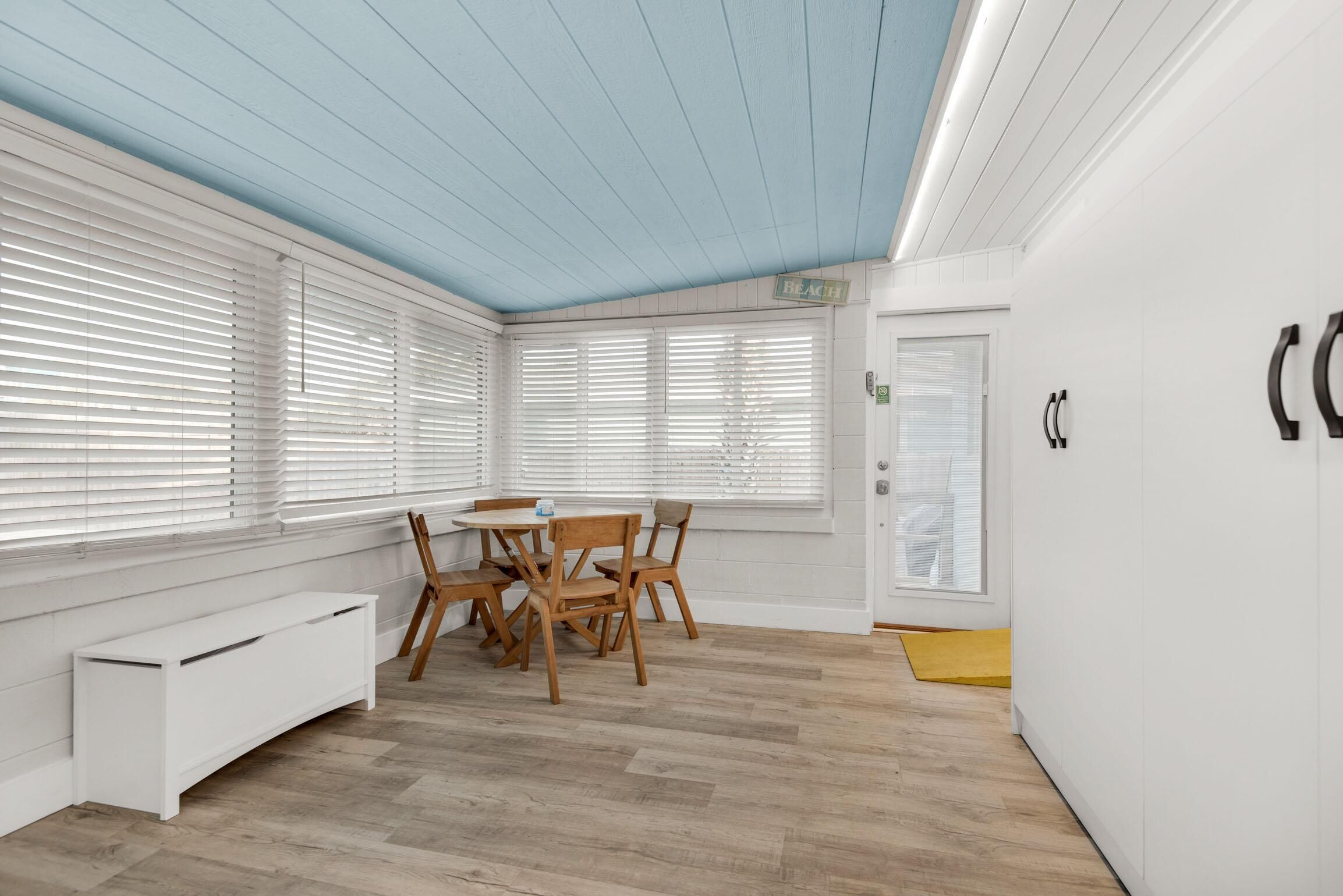 A room with a wooden table and chairs, a white bench, and a window with blinds.