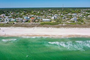 Vue aérienne d’une ville côtière avec une plage, des maisons et un ciel dégagé.