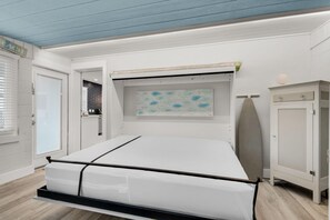 Une pièce comprenant un lit, une petite armoire, une planche de surf et une œuvre d’art accrochée au mur.