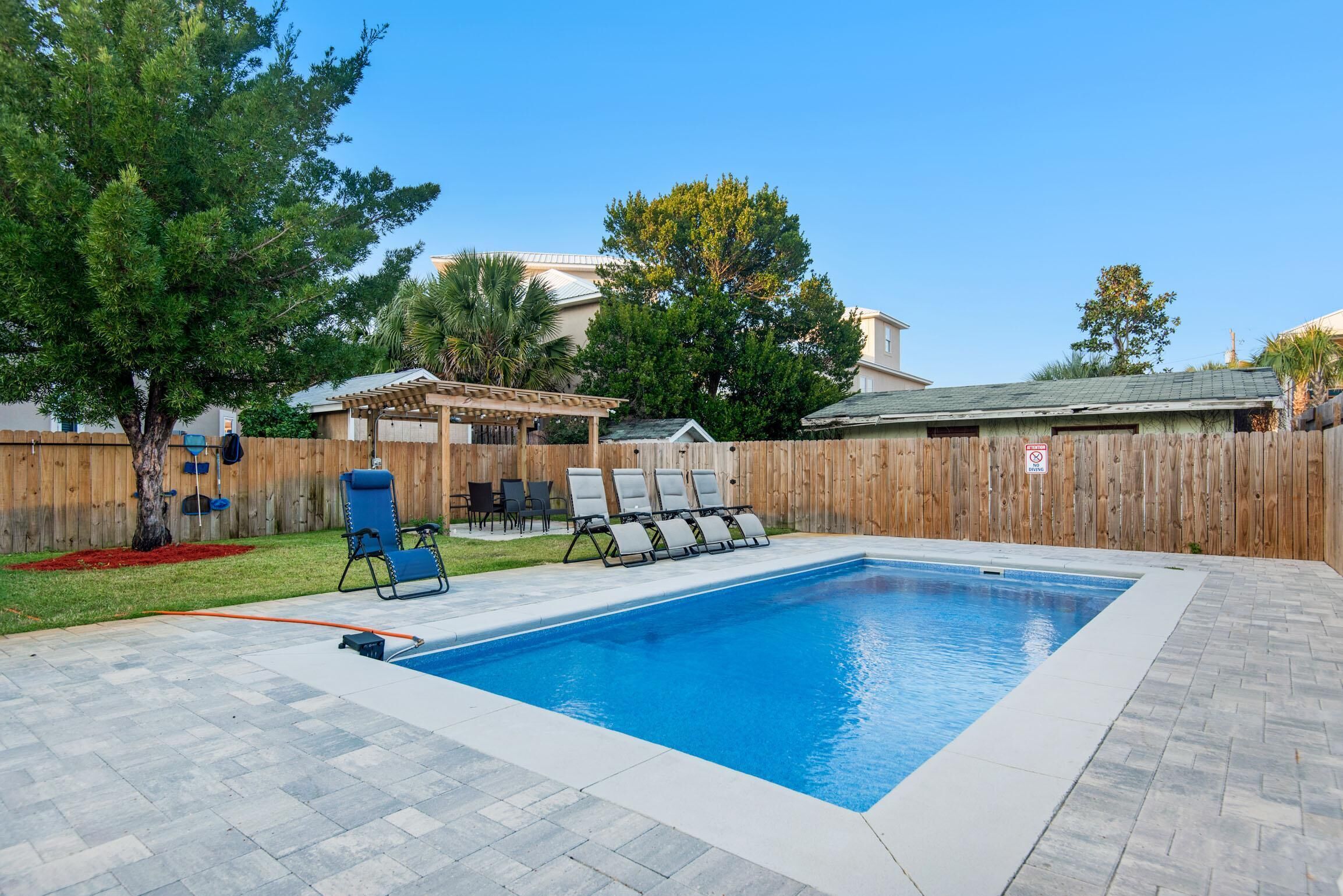 Una piscina rectangular con cubierta de madera, rodeada por un cerco de madera y un área de patio techada con sillas.