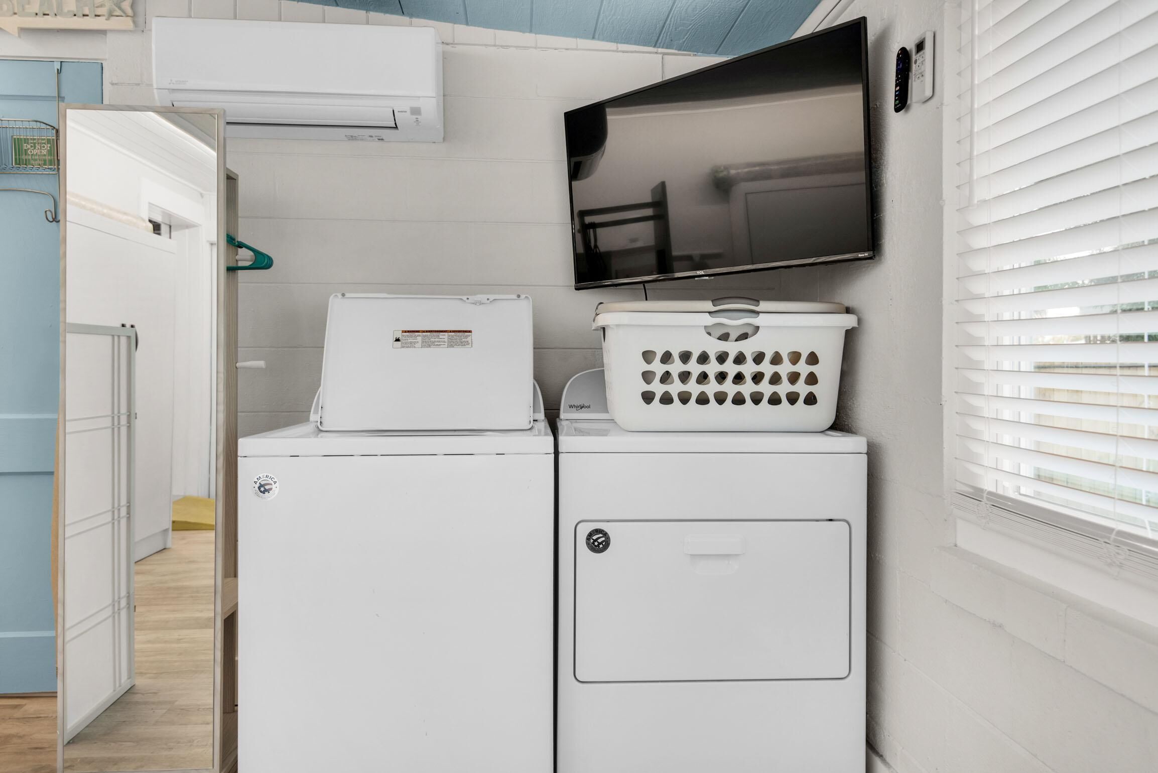A laundry area with a washer and dryer, a television mounted on the wall, and a window with blinds.