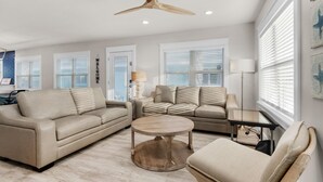 A modern living room with a beige sofa, a round coffee table, and a ceiling fan. - Emerald Flamingo (Panama City Beach)