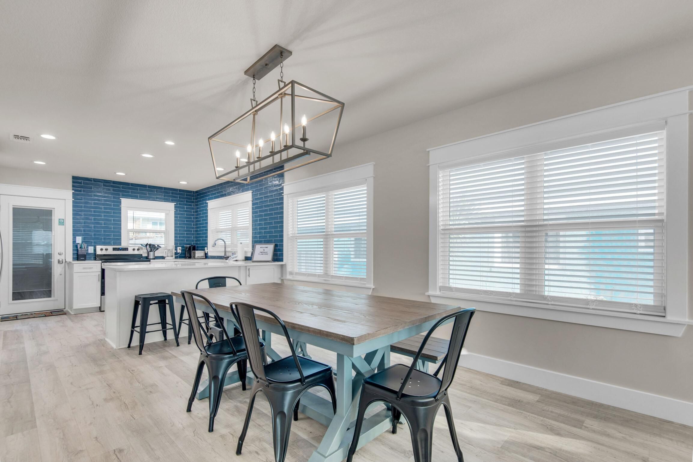 Een moderne keuken met een centraal eiland, een zithoek met stoelen en grote ramen met zonwering.