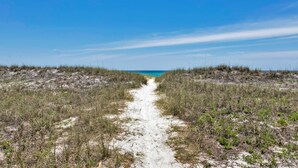 A sandy path leading to a beach with sparse vegetation on either side. - Emerald Flamingo (Panama City Beach)