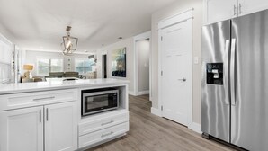 A modern kitchen with white cabinetry, a stainless steel refrigerator, a built-in microwave, and a pendant light. - Emerald Flamingo (Panama City Beach)