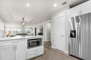 A modern kitchen with white cabinetry, a stainless steel refrigerator, a built-in microwave, and a pendant light. - Emerald Flamingo (Panama City Beach)