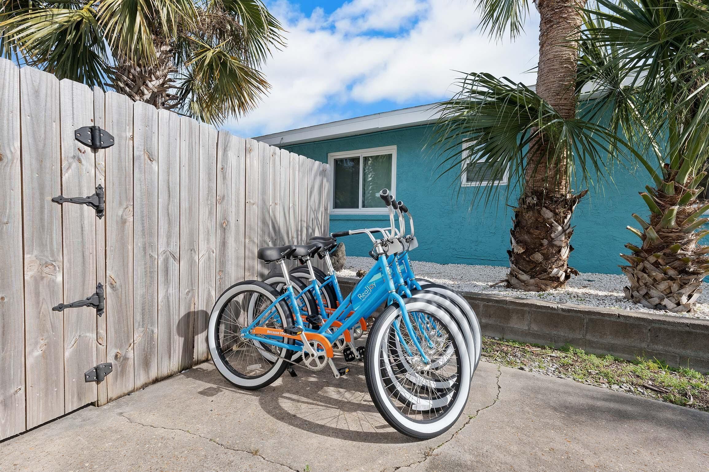 A blue bicycle parked against a wooden fence with a house in the background.