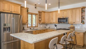 Una cocina moderna con armarios de madera, electrodomésticos de acero inoxidable, una isla grande con taburetes de bar y una ventana que proporciona luz natural.