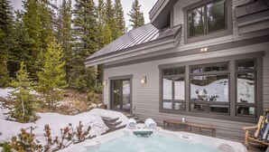 Una casa moderna con jacuzzi en el jardín, rodeada de nieve y árboles.