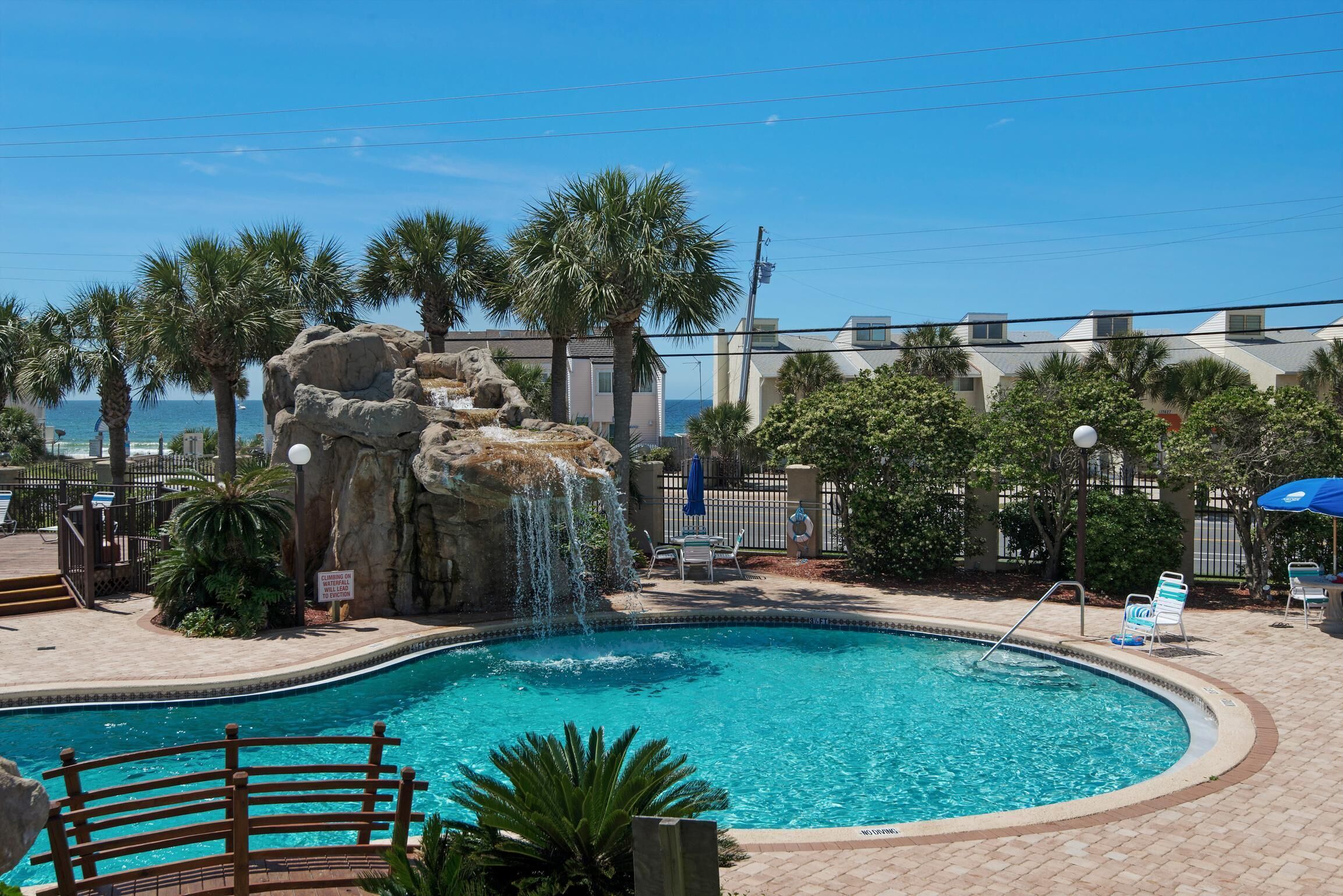 A pool with a waterfall feature, surrounded by palm trees and a view of the ocean.