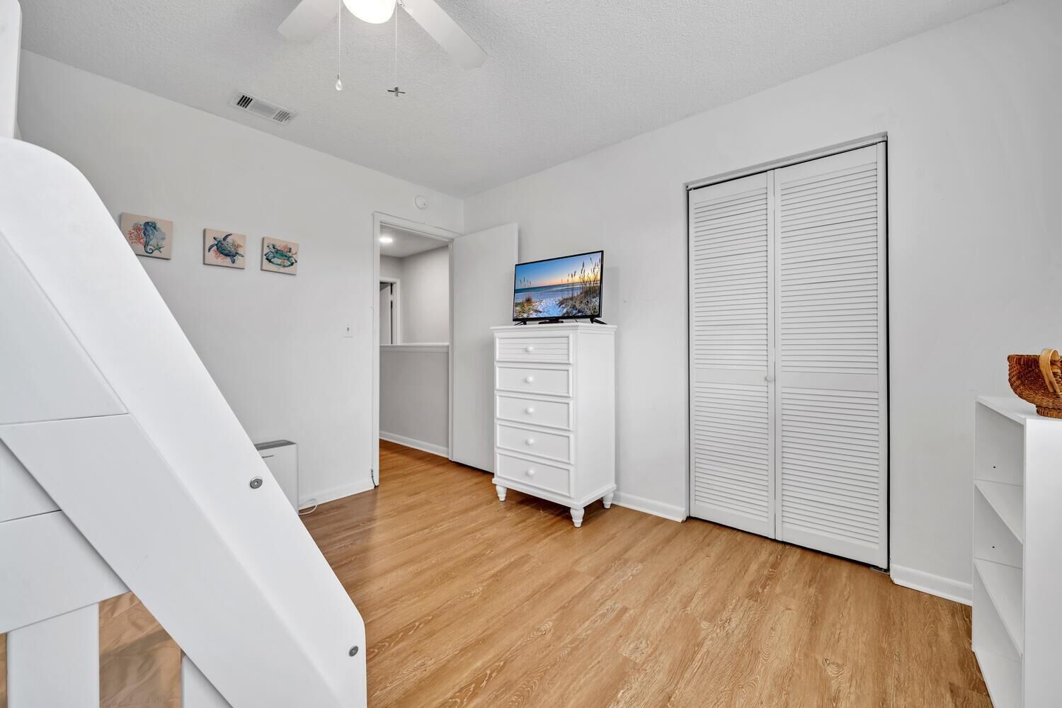 A hallway with a white dresser, a television on a stand, and a white closet.