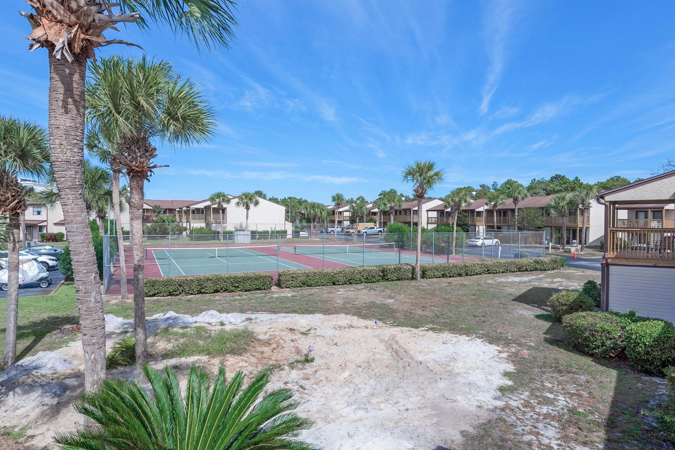 A tennis court surrounded by palm trees and residential buildings.