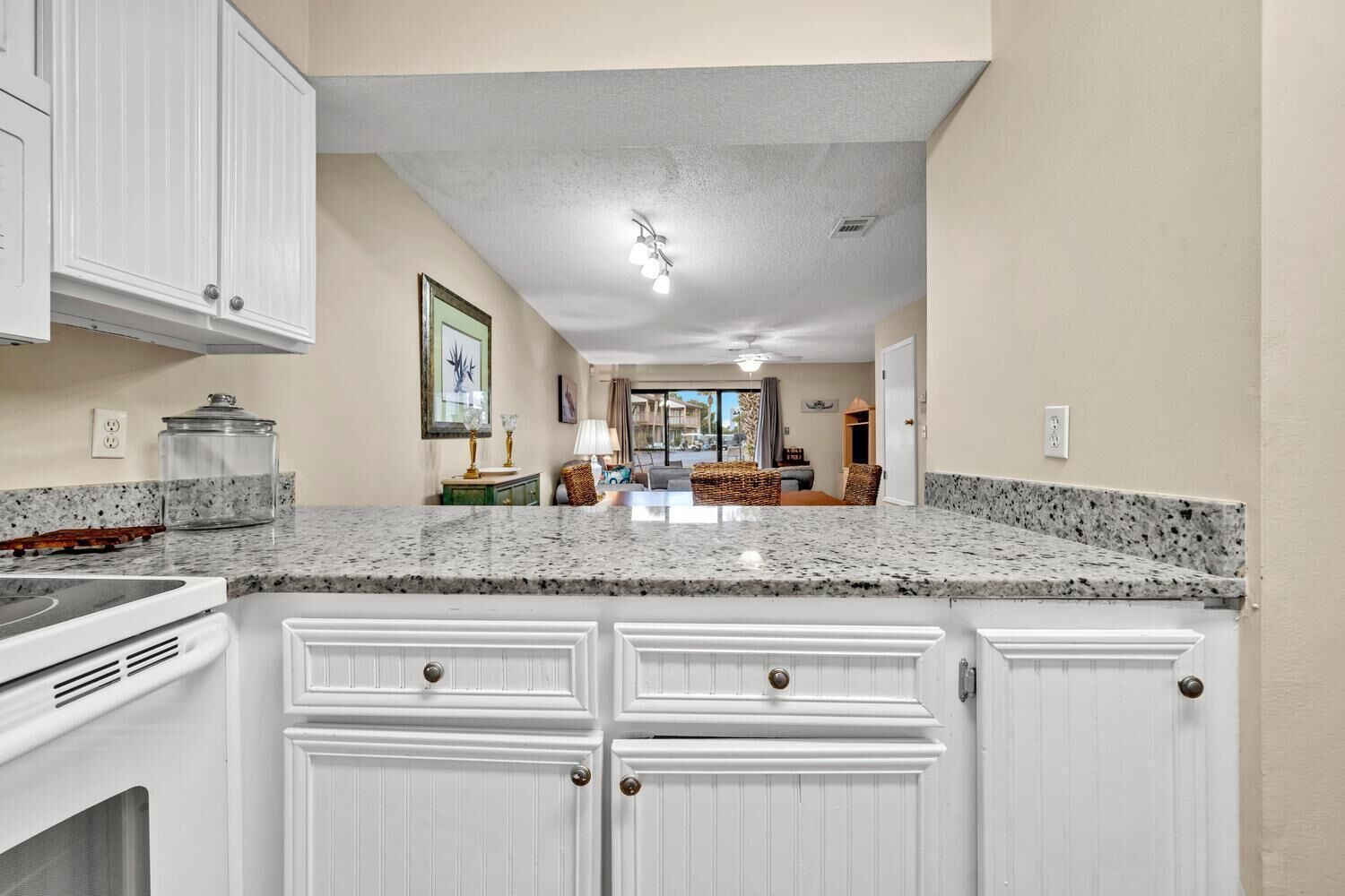 A kitchen with white cabinetry, granite countertops, and a view into the living area.