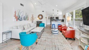A modern living room with a white sofa, a blue armchair, and a red sofa. There is a kitchen in the background with a large window.