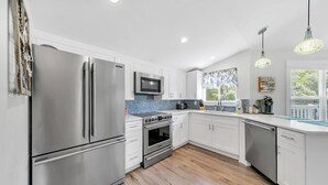A modern kitchen with stainless steel appliances, white cabinetry, and a blue-tiled backsplash.