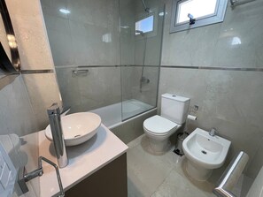 A modern bathroom with a glass-enclosed shower, a bathtub, a toilet, and a bidet.