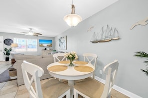 A dining area with a round table, white chairs, and a vase of flowers. - Beach Dream (Miramar Beach)