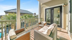 A balcony with wicker furniture, a sliding glass door, and a view of a building with a metal roof. - Redfish Village M1222 (Santa Rosa Beach)