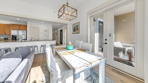 A modern kitchen with wooden cabinets, a central island, and a dining area with a white table and grey sofa. - Redfish Village M1222 (Santa Rosa Beach)