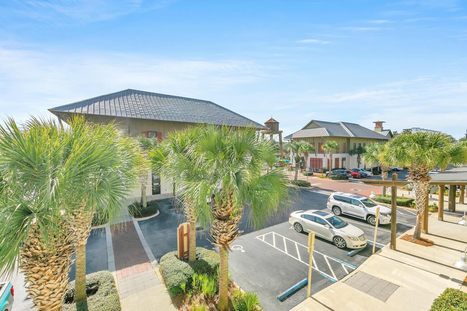 A hotel with a parking lot, palm trees, and a building with a sloped roof.