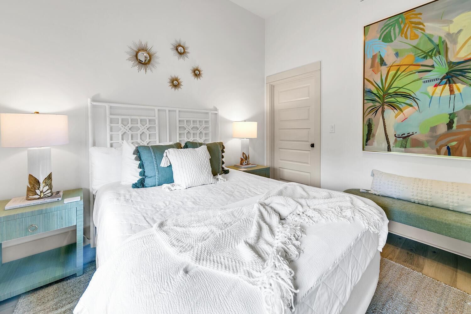 A bedroom with a large bed, two bedside tables, a nightstand, a door, and a painting on the wall.